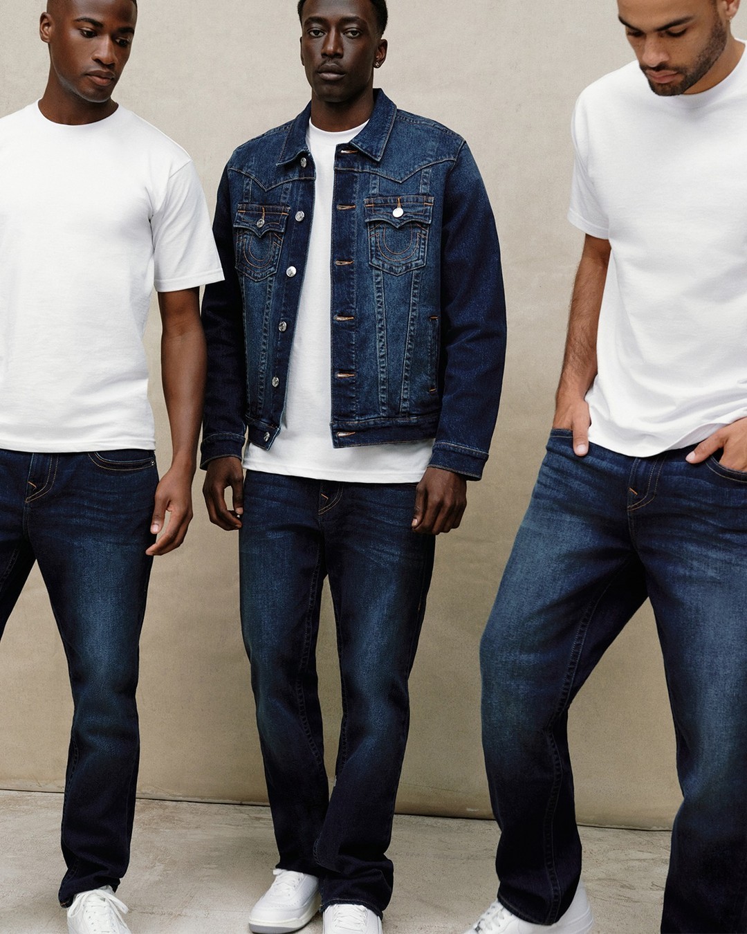 Three male models in jeans and white shirts posed casually against a tan backdrop.